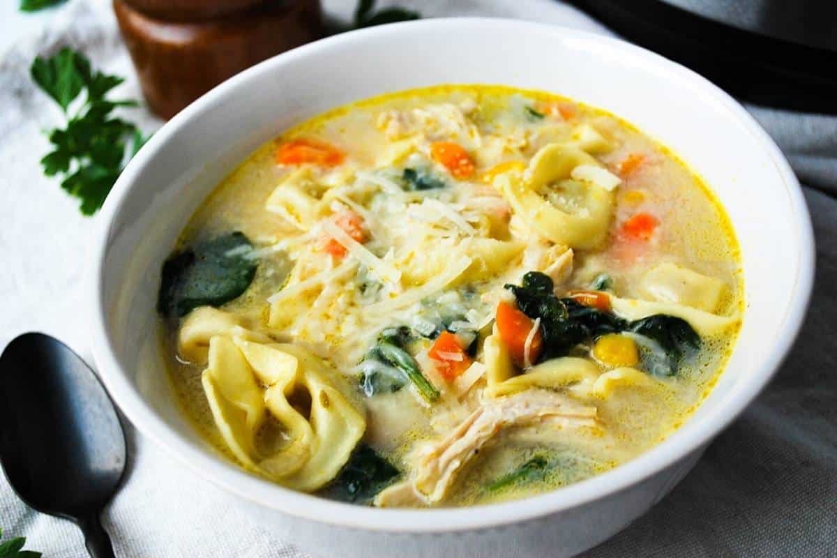 creamy tortellini soup with chicken in a white bowl with a spoon next to it