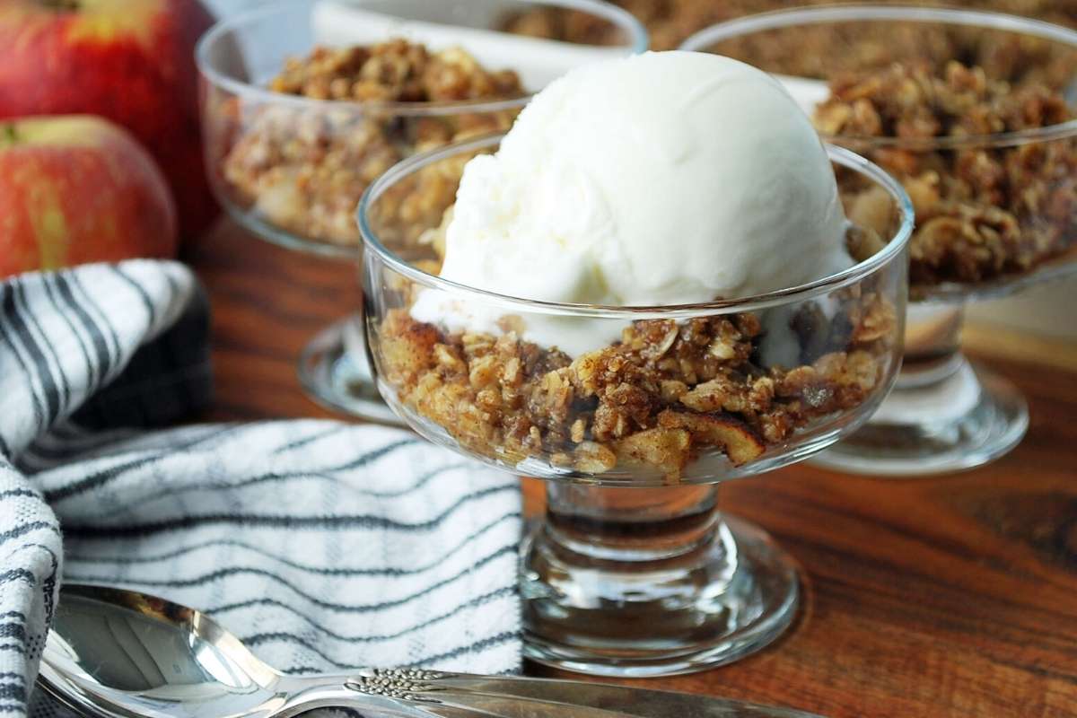 dessert dishes of apple crisp with napkin and apples in the background