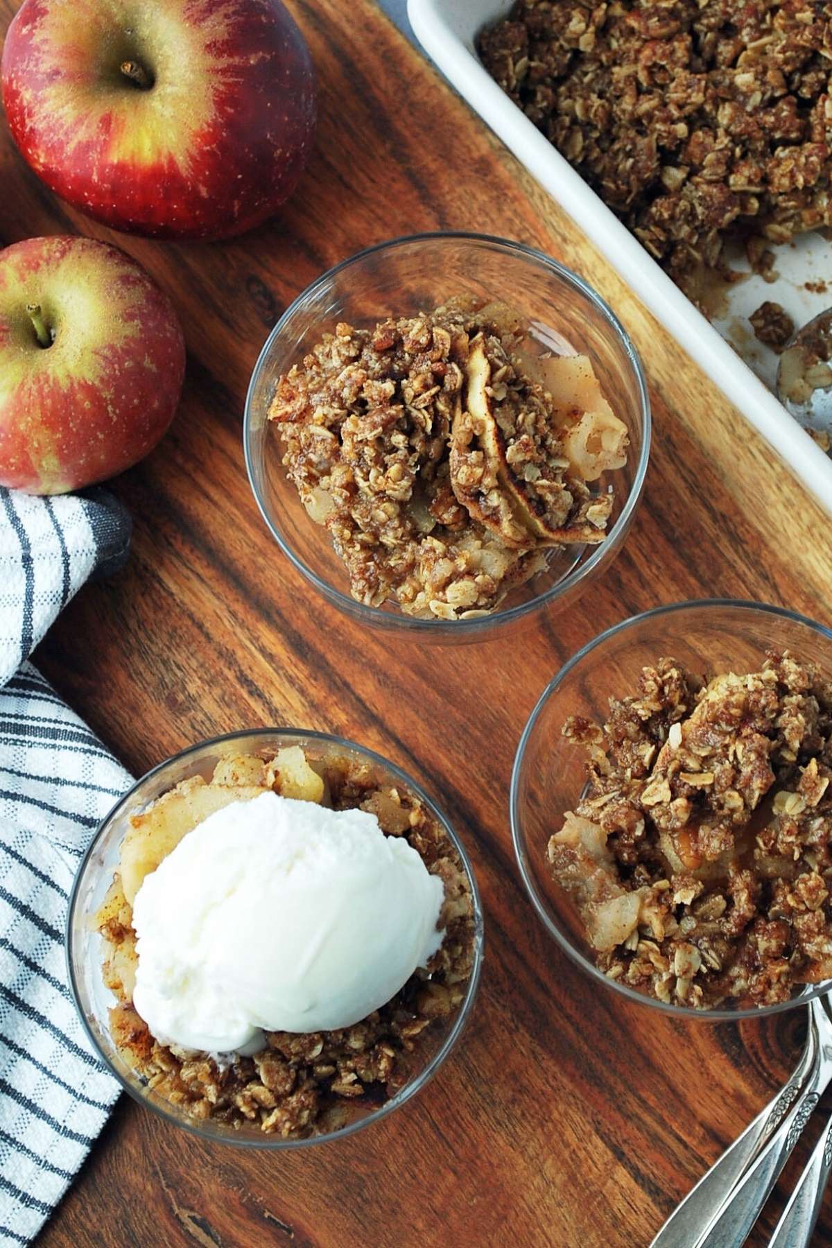 wooden tray with parfait dishes of apple crisp and an apple in the background