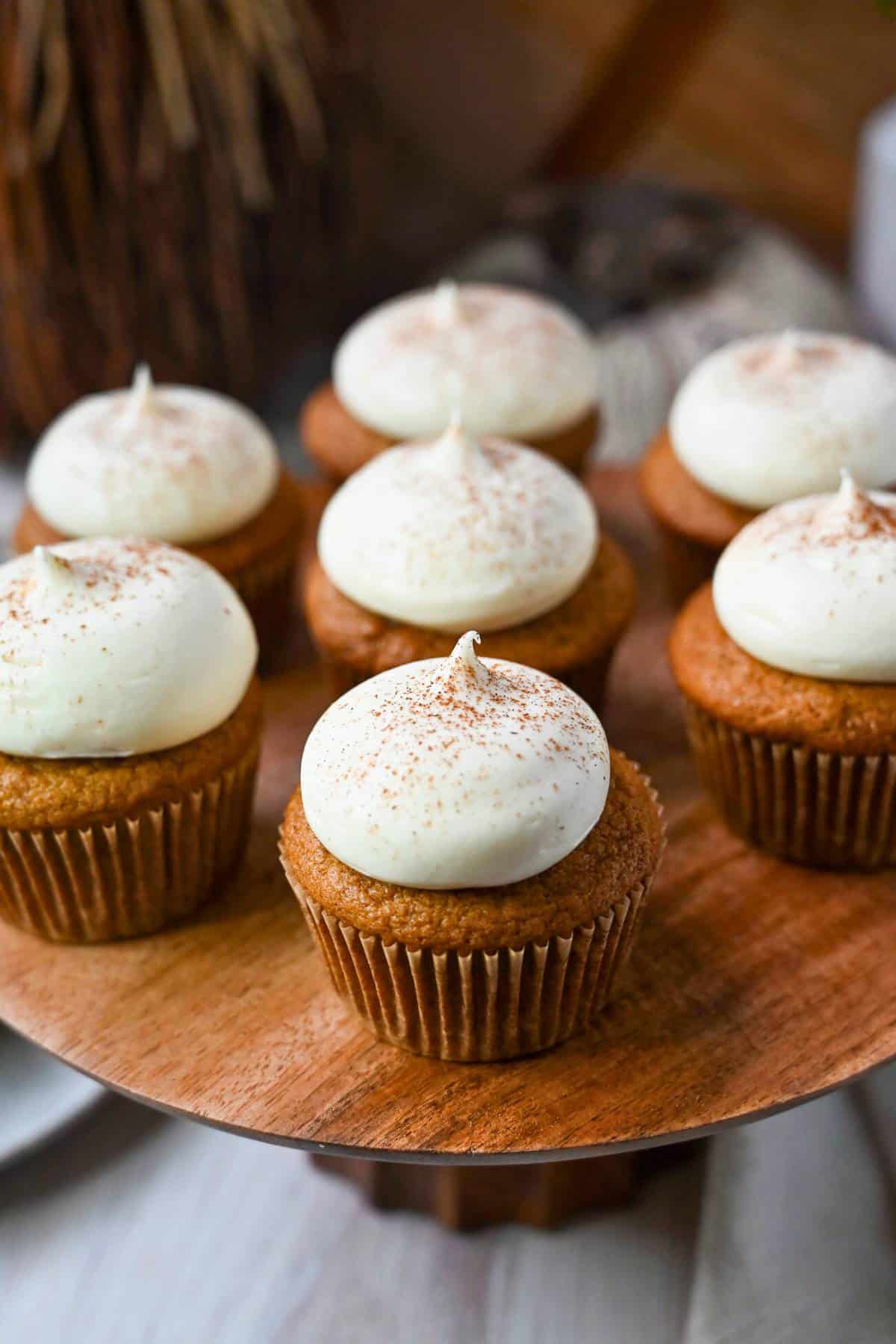 a platter of frosted pumpkin cupcakes with fall decor around it