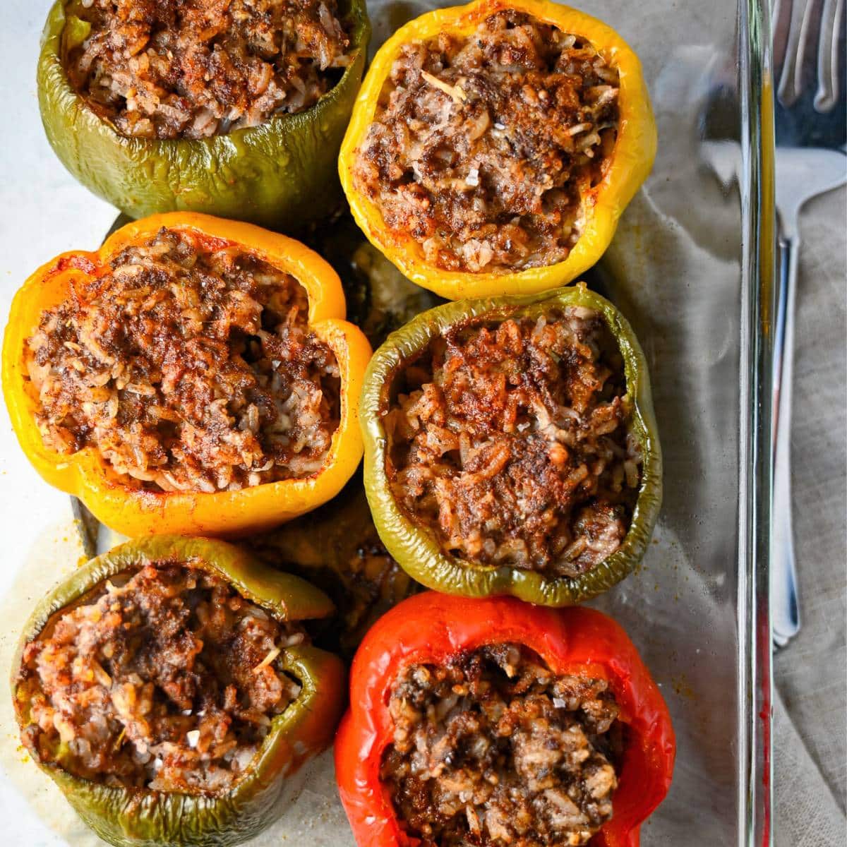 six stuffed peppers baked in a glass dish on top of a cloth napkin
