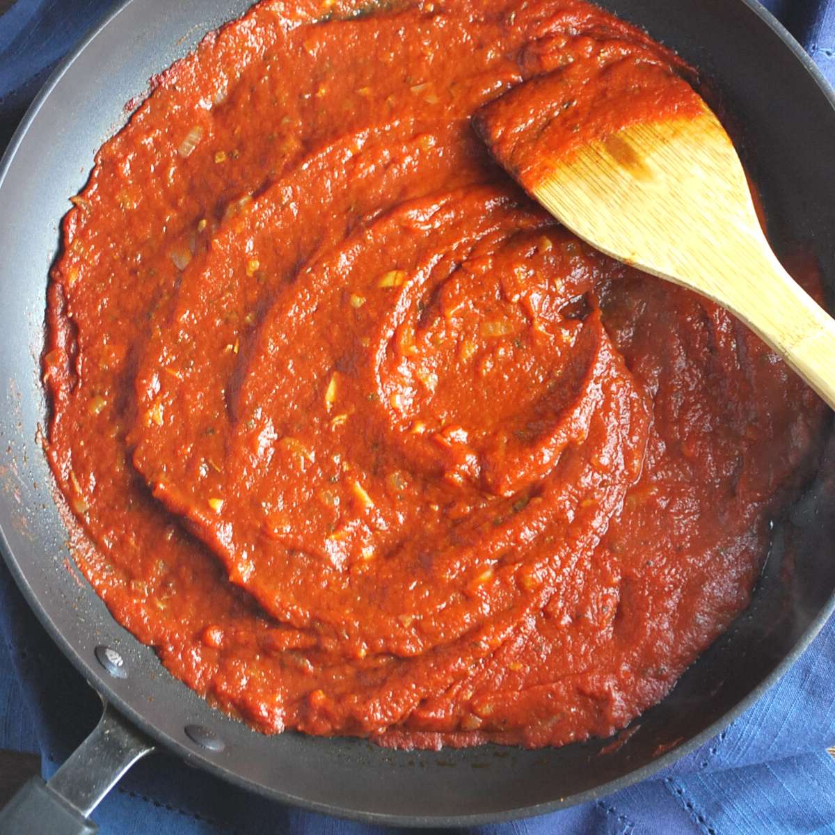 overhead photo of a skillet of san marzano pizza sauce with a wood spoon