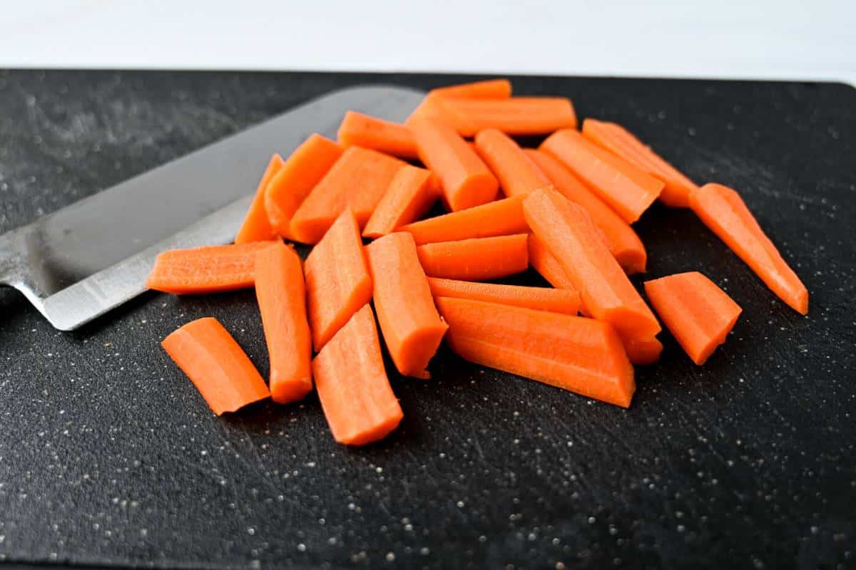 chopped carrots on a black cutting board with a knife