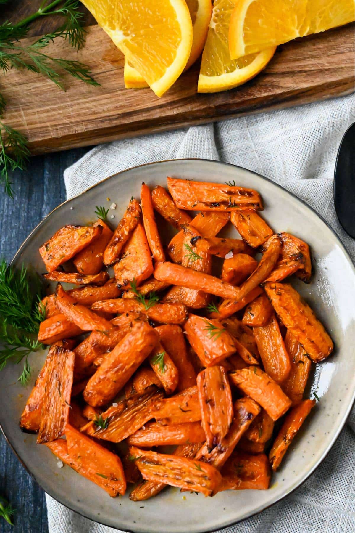 air fryer carrots on a plate with a napkin underneath and sliced oranges behind it