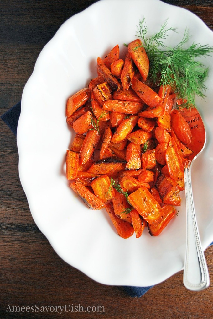 Overhead photo of roasted carrots with fresh dill in a white serving dish with a spoon