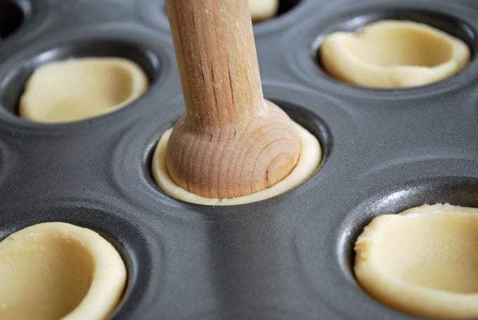 A close up of a tart tamper pressing down on tart dough in a mini muffin pan