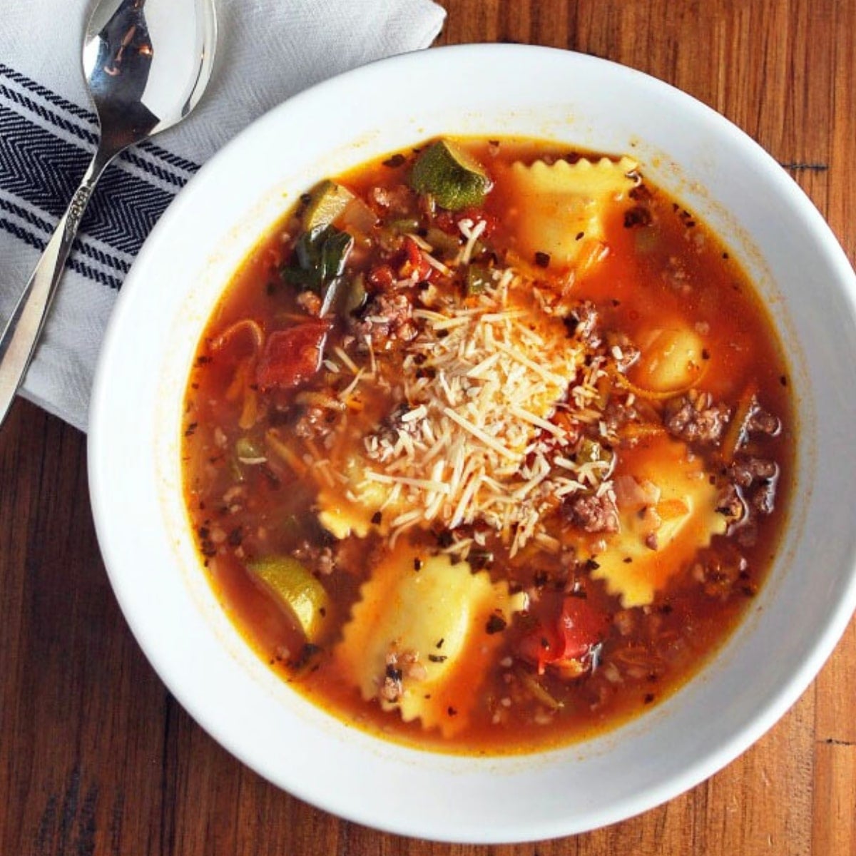 a bowl of ravioli sausage soup with a napkin and spoon
