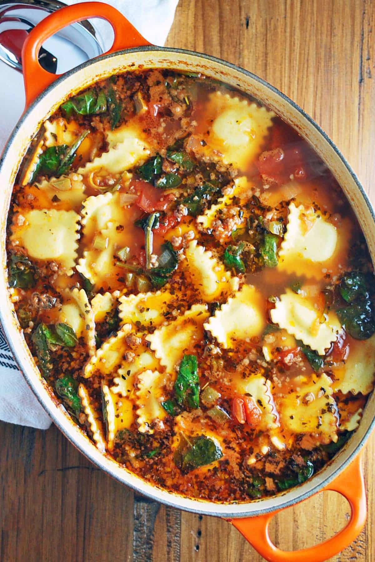 looking down at a Dutch oven of ravioli soup with sausage and vegetables