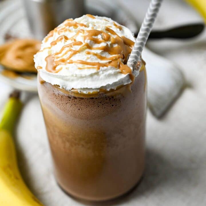 close up photo of a pb chocolate banana protein shake topped with whipped cream and peanut butter in a glass with a straw