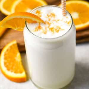 close up of a creamsicle orange protein smoothie in a glass with orange zest, an orange slice and a straw