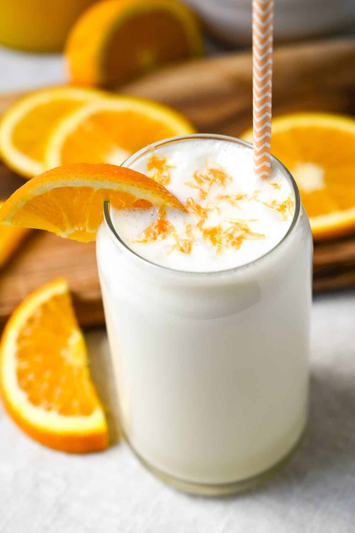 A creamsicle smoothie in a glass with an orange straw and zest on top