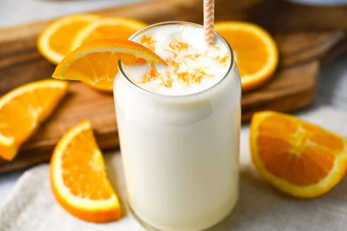 a creamsicle protein shake in a glass with orange slices around it