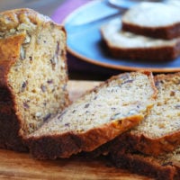 Sliced date nut quick bread on a cutting board with a plate of buttered bread in the background