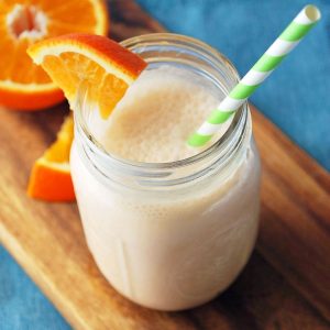 orange creamsicle shake in a mason jar on top of a wood cutting board with orange slices