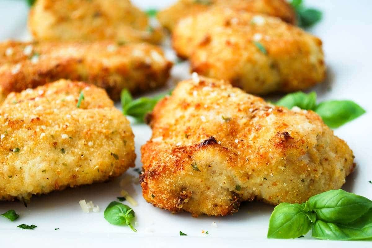 platter of air fryer parmesan crusted chicken breasts garnished with fresh basil sprigs