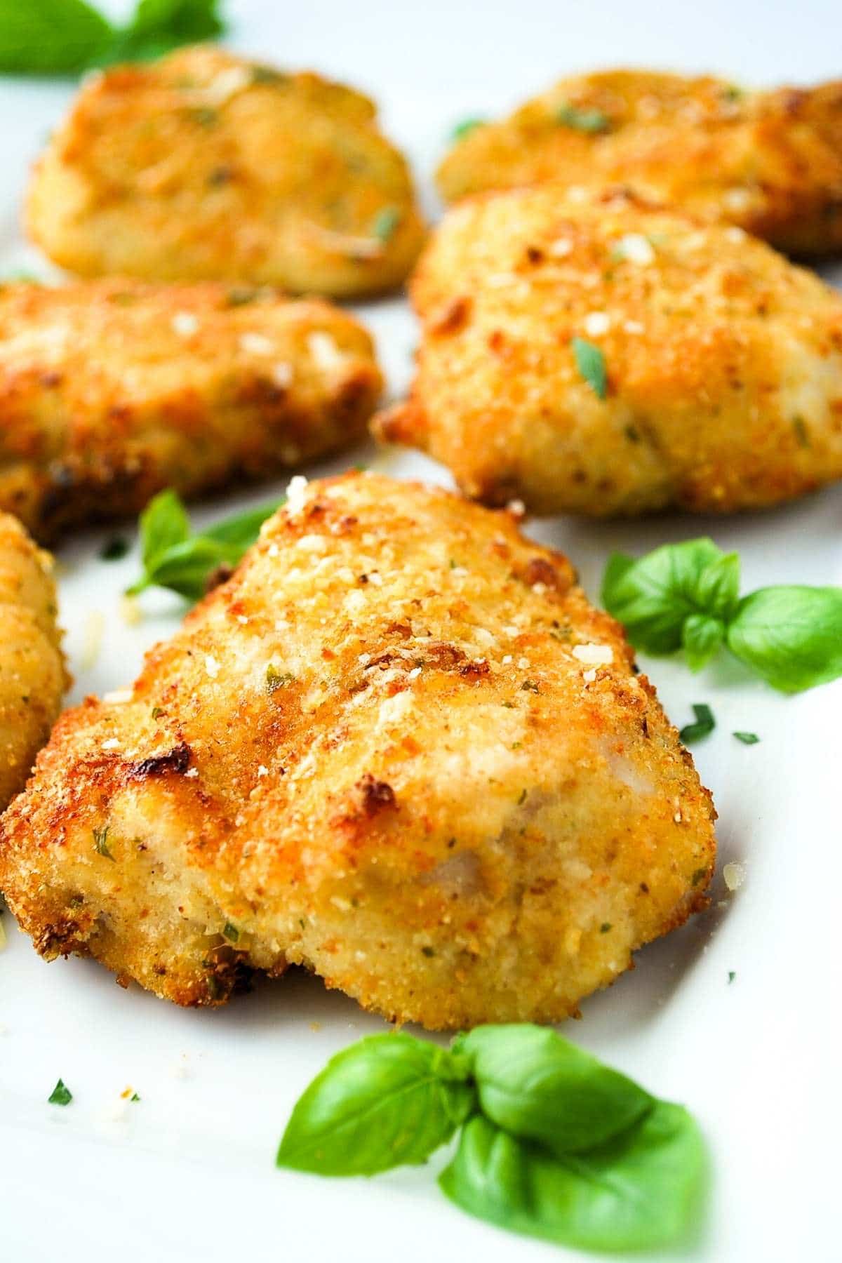 air fryer parmesan chicken on a white platter with fresh basil