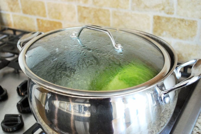 a head of cabbage cooking in a pot with a loosely covered lid