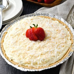 overhead photo of a coconut cream pie with a whole strawberry one top with a plate and spoon next to it