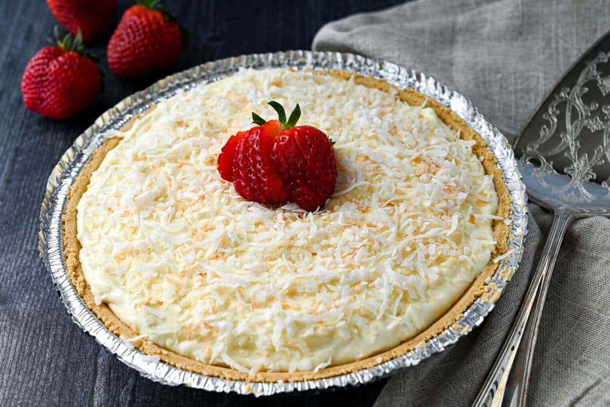 coconut pie with a serving spatula and strawberries in the background
