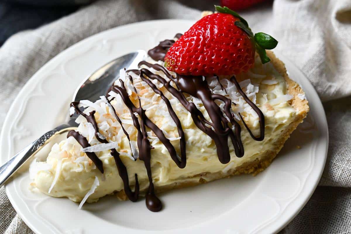 a slice of no bake coconut pie drizzled in chocolate with a slice of strawberry on a plate with a spoon