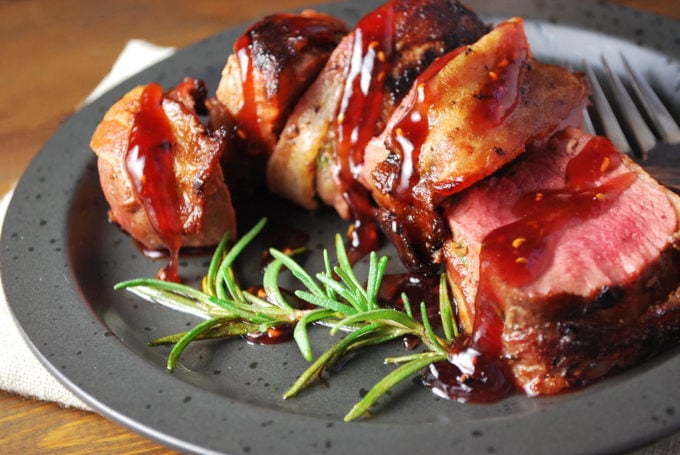 A plate of sliced Venison with raspberry sauce drizzled on top