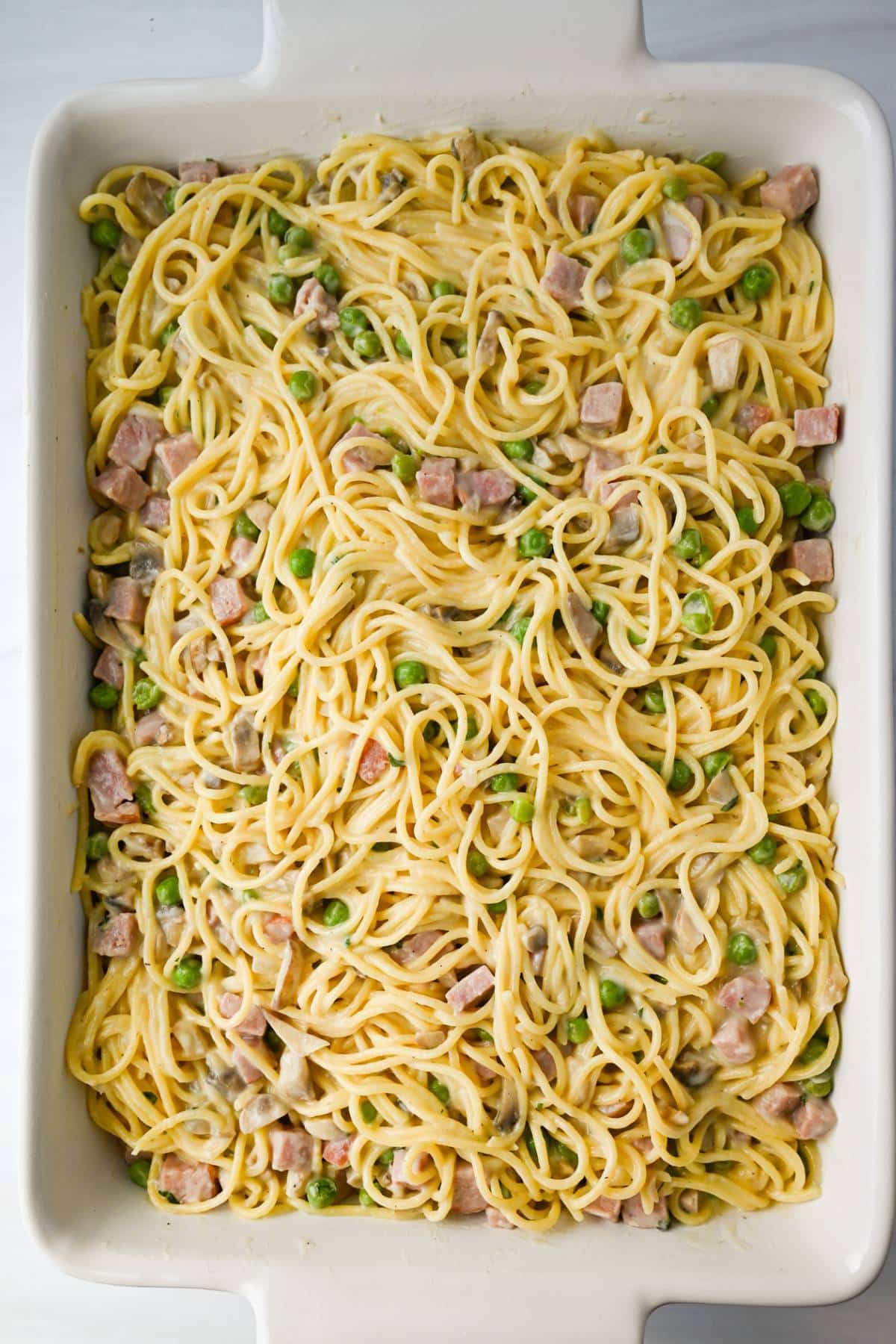 creamy spaghetti with ham and peas in a casserole dish