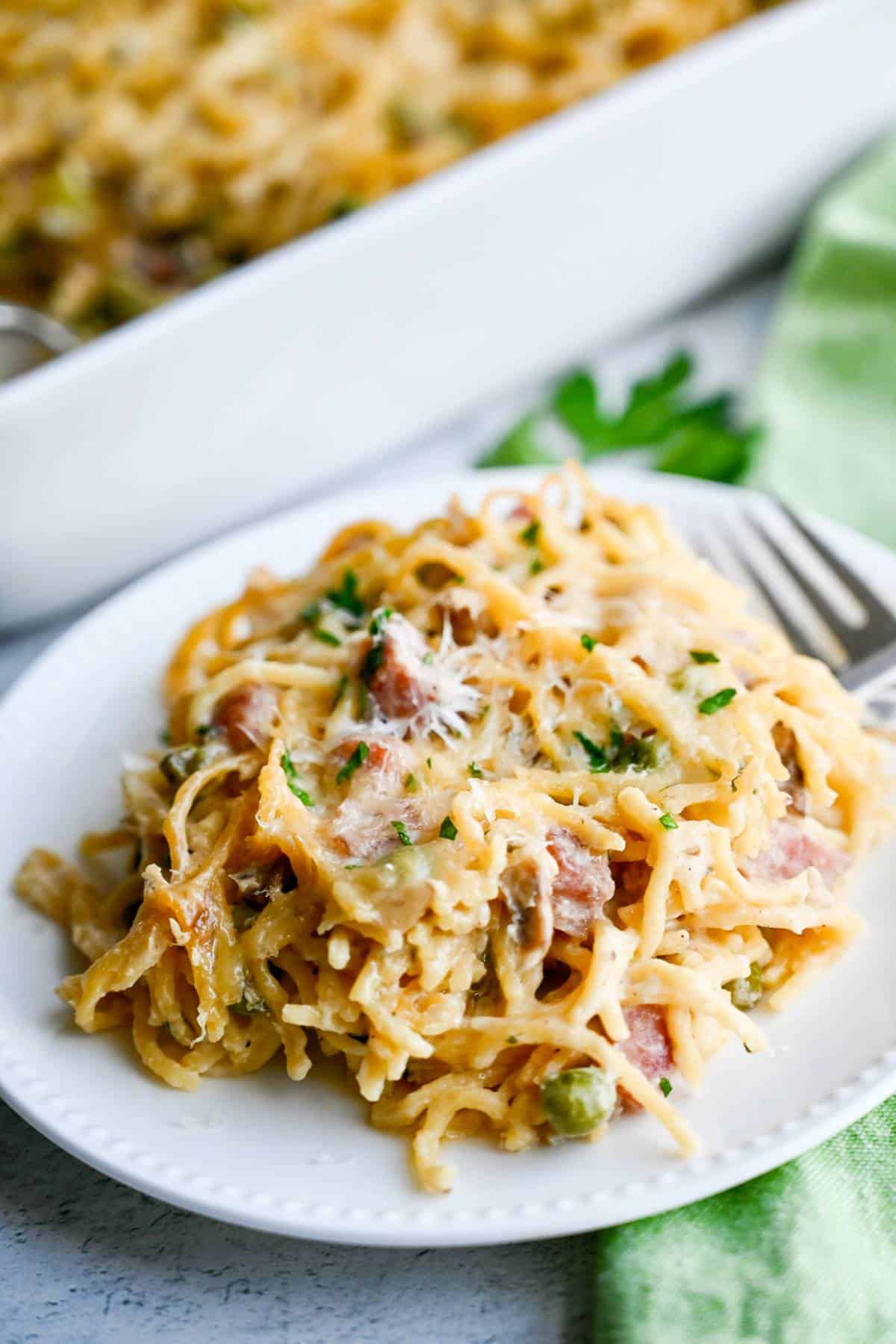 ham spaghetti casserole with peas on a plate with the casserole dish in the background