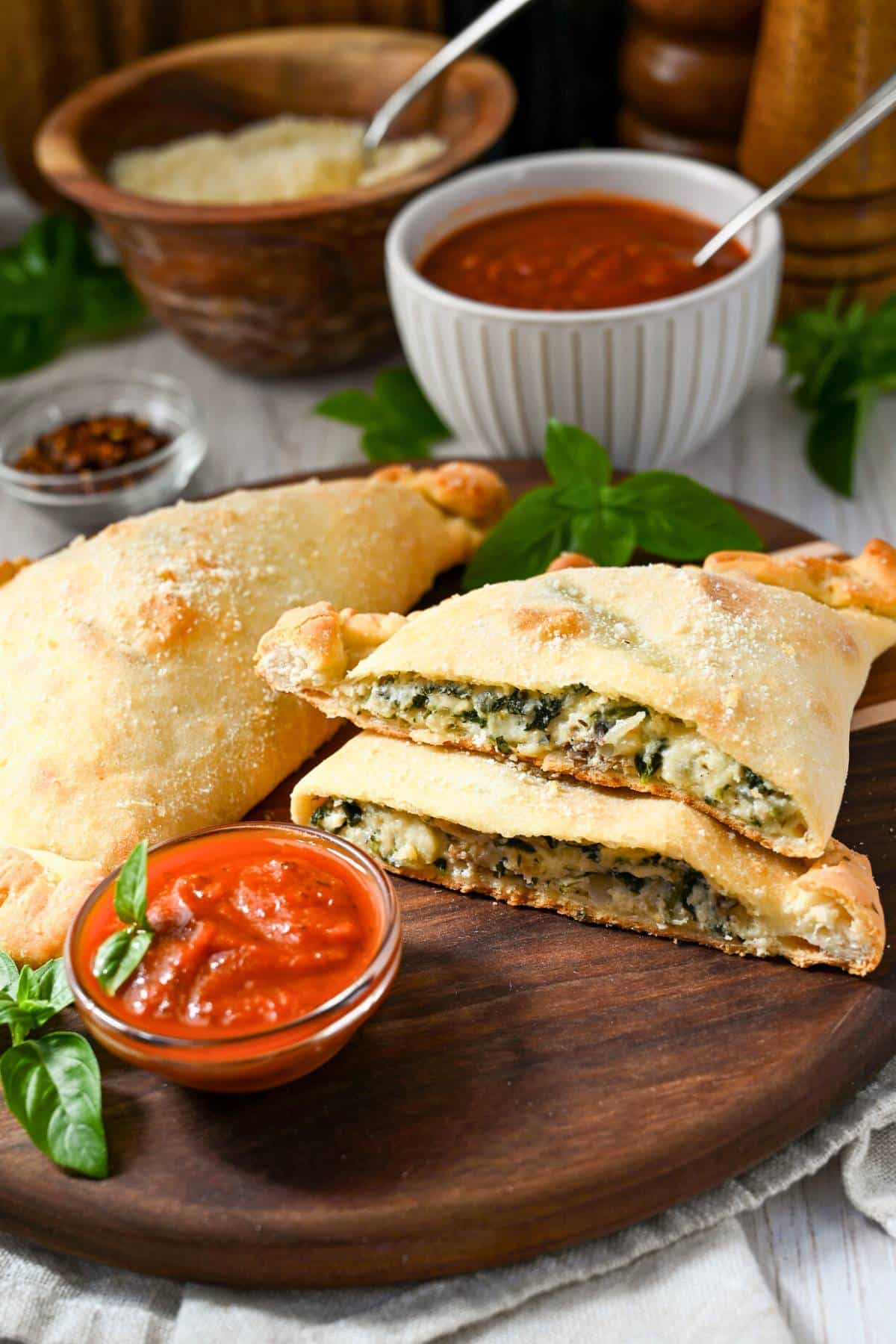 a sliced spinach calzone on a cutting board with a whole calzone and dish of marinara