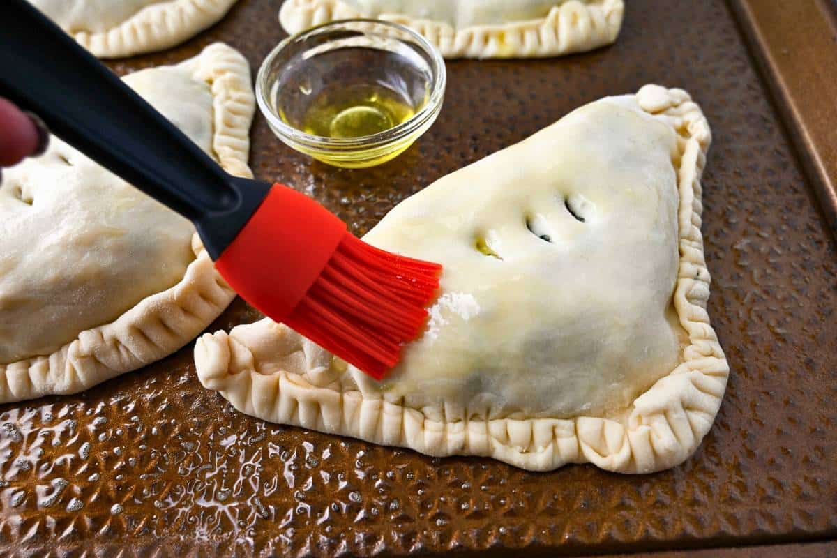 brusing olive oil on top of a calzone on a baking sheet