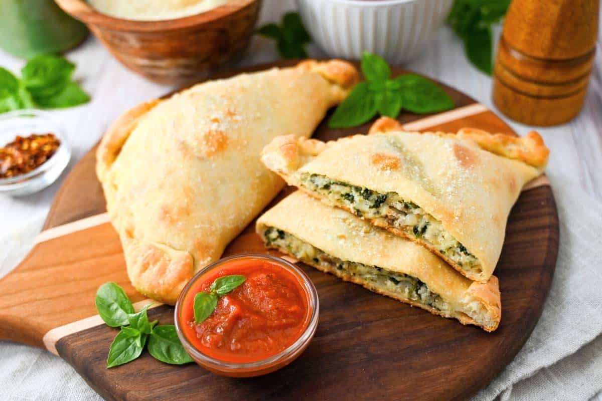 a whole calzone and a sliced calzone and a dish of marinara