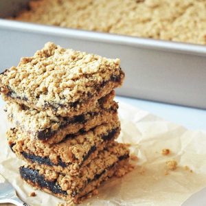 four oatmeal date bars stacked on parchment paper with the pan of sliced bars in the background