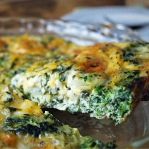 close up of a slice of spinach quiche raised from the dish with a spatula