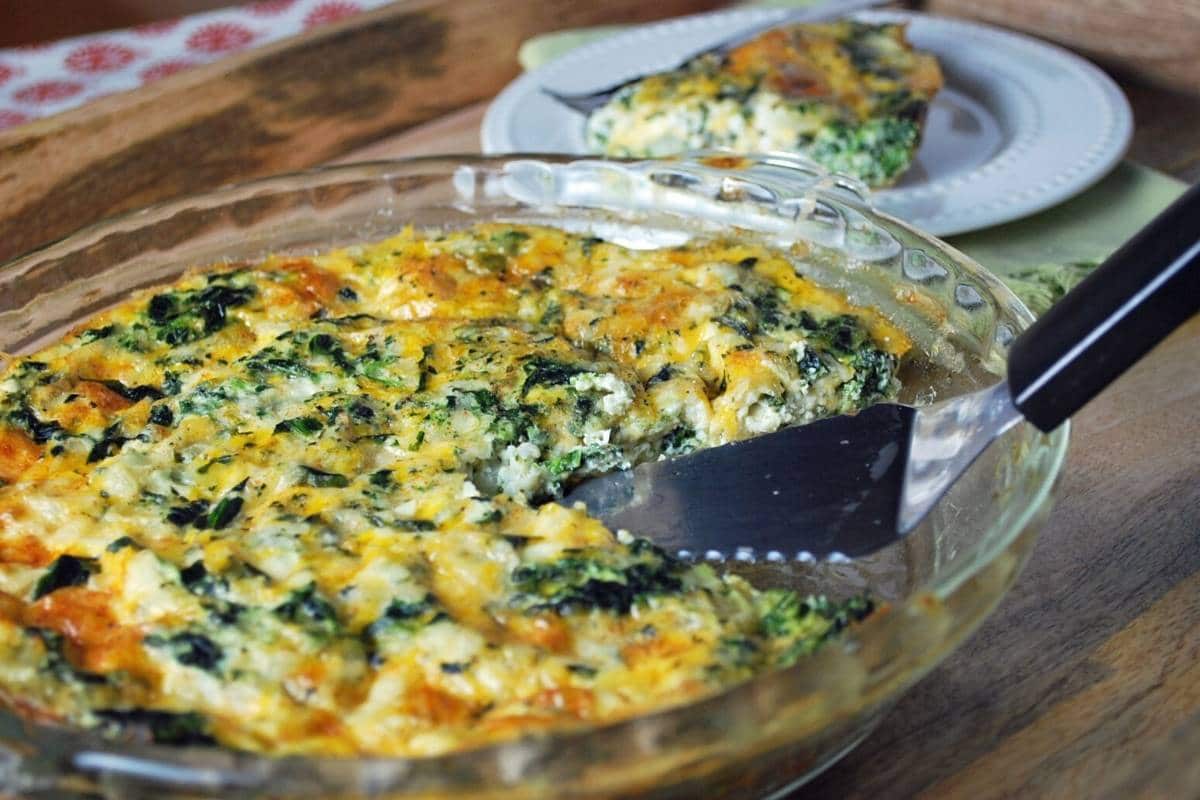 a pan of spinach quiche on a tray with a slice of quiche on a plate