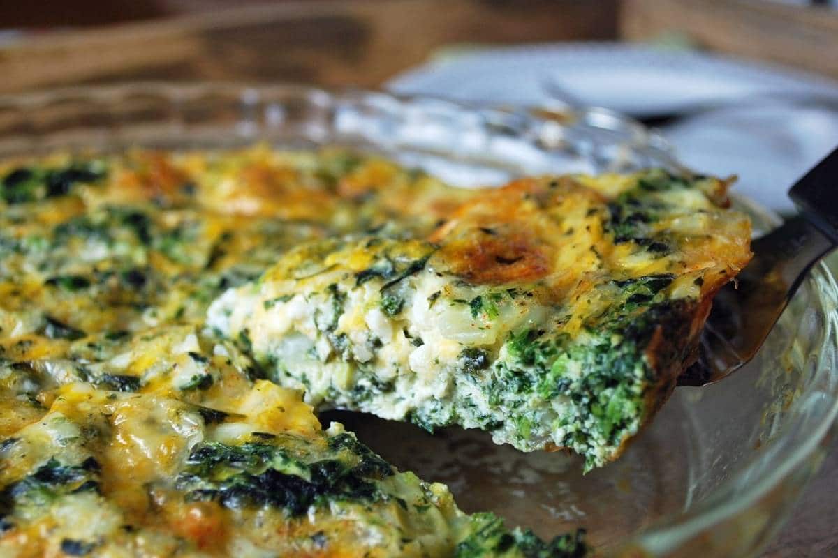 a raised slice of crustless spinach quiche in a pie plate