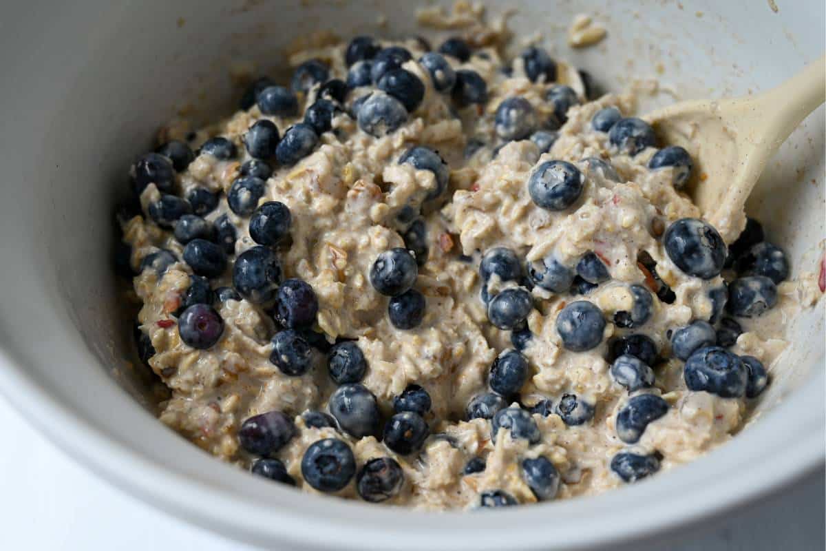 swiss oats with fresh blueberries stirred together in a white bowl with a spoon