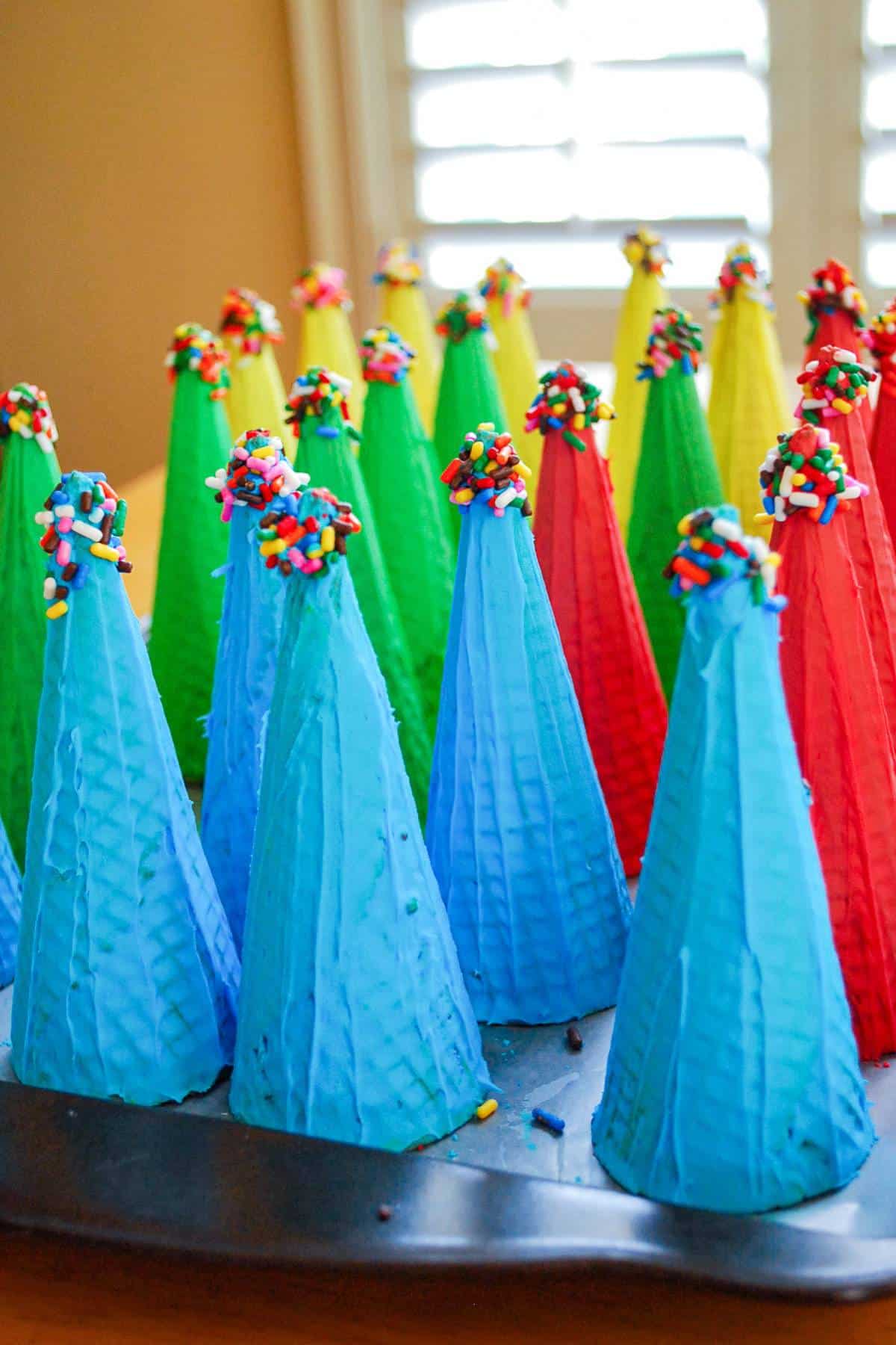 ice cream cones painted with colored frosting with the tips dipped in sprinkles