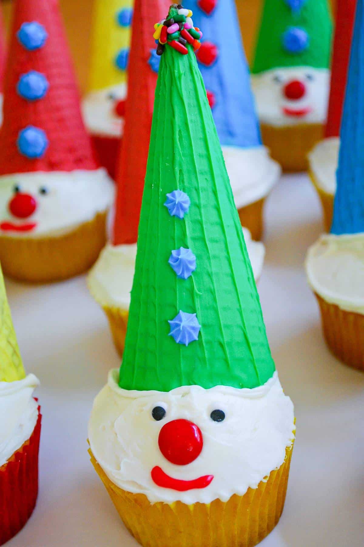 close up of a clown cupcake with a green ice cream cone hat painted with frosting
