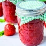 jars of freezer jam next to a fresh strawberry