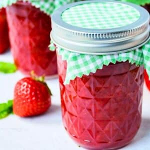 jars of freezer jam next to a fresh strawberry