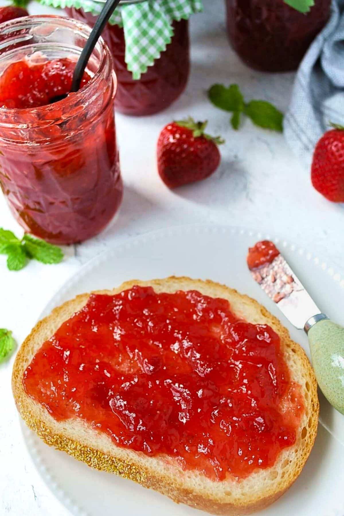 jam on toast with jars of strawberry jam behind it