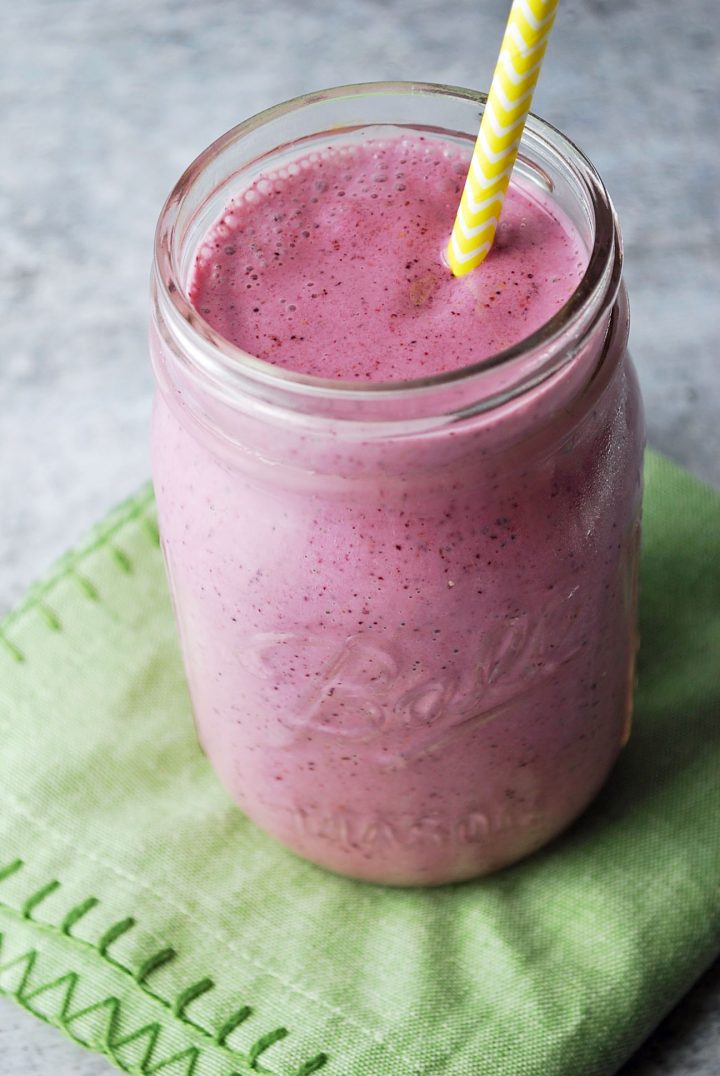 berry smoothie in a mason jar with yellow straw and green napkin underneath