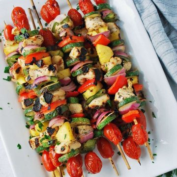 overhead photo of chicken kabobs on a white platter with a napkin underneath