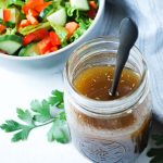 maple balsamic vinaigrette dressing in a jar with a spoon and a salad in the background