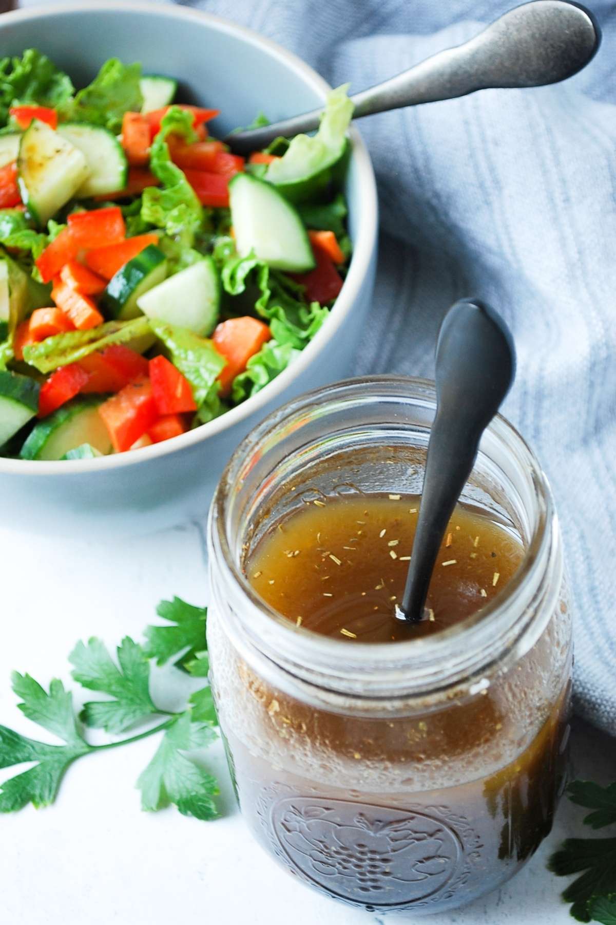 A jar of balsamic vinaigrette with a spoon and a bowl of salad in the background