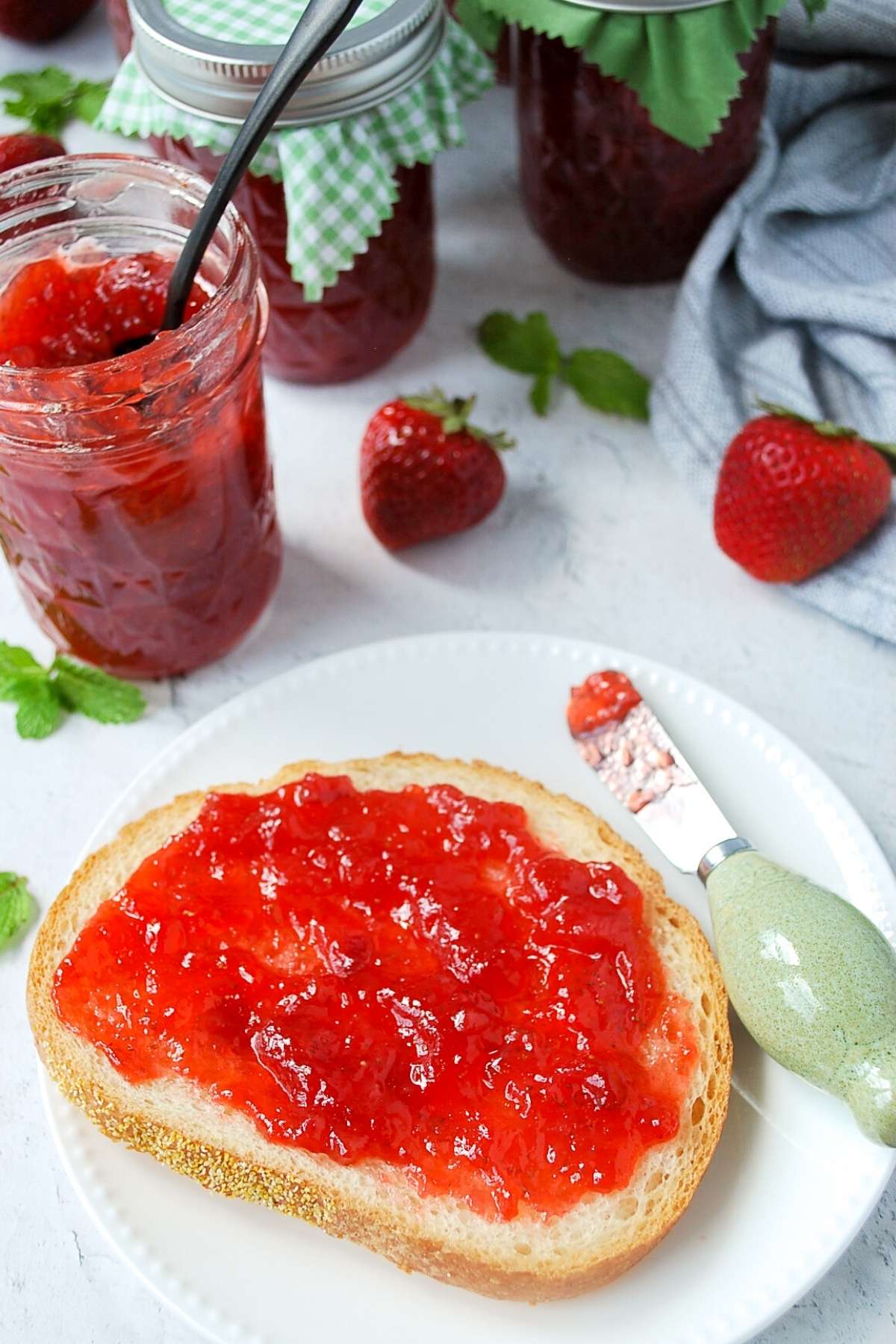 overhead photo of toast with strawberry jam and jars of strawberry jam in the background