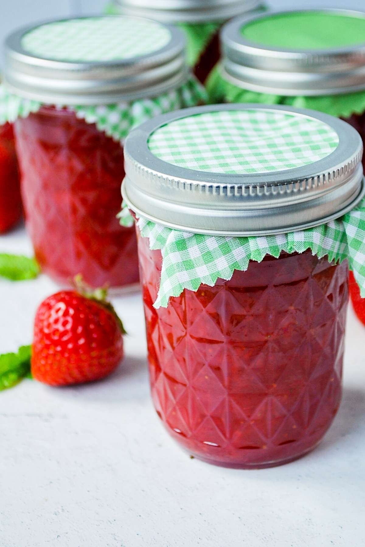jars of strawberry jam with a fresh strawberry 