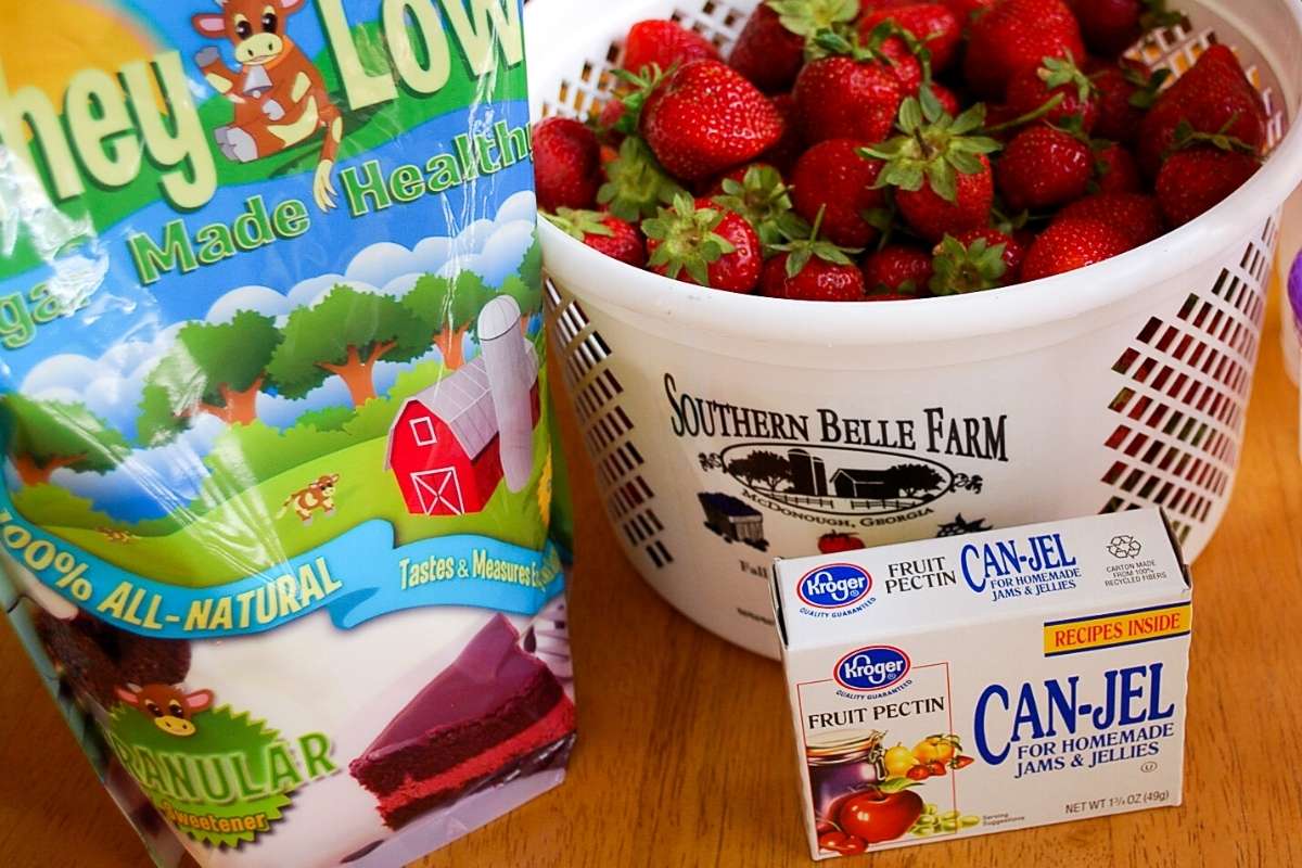 Whey-Low sugar, fresh strawberries in a bucket, and a box of pectin mix
