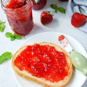 toast with jam and a knife with a jar of strawberry jam in the background
