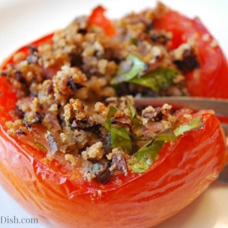 A close-up of a stuffed half tomato being sliced with a fork