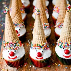 clown cupcakes with sugar ice cream cone hats on a wood platter with sprinkles